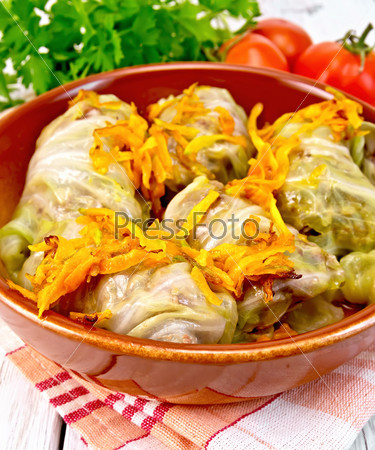 Stuffed cabbage meat in cabbage leaves with roasted carrots in a brown ceramic pan on a napkin, tomatoes, parsley on a light background boards