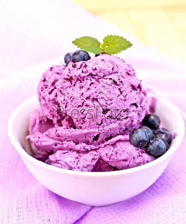 Blueberry ice cream with mint and berries in a bowl on a purple napkin on a wooden boards background
