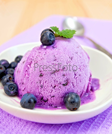 Blueberry ice cream with mint and berries in a plate on a background of purple cloth and wooden planks
