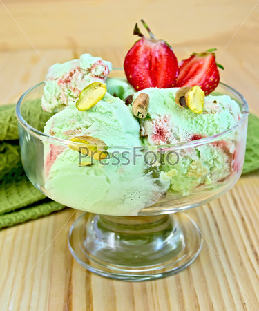 Ice cream strawberry pistachio in a glass goblet with strawberries and pistachios with a napkin on a wooden boards background