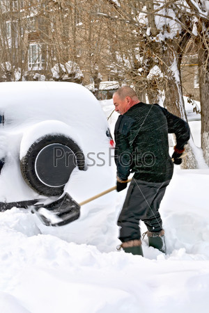 A man with a shovel digs up your car in the snow, stock photo