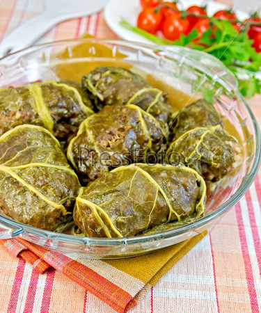 Stuffed cabbage with meat and rhubarb leaves in a glass dish, parsley, tomatoes on a cloth background