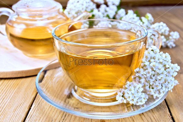 Yarrow tea in a glass cup and teapot, fresh yarrow flowers on a wooden boards background