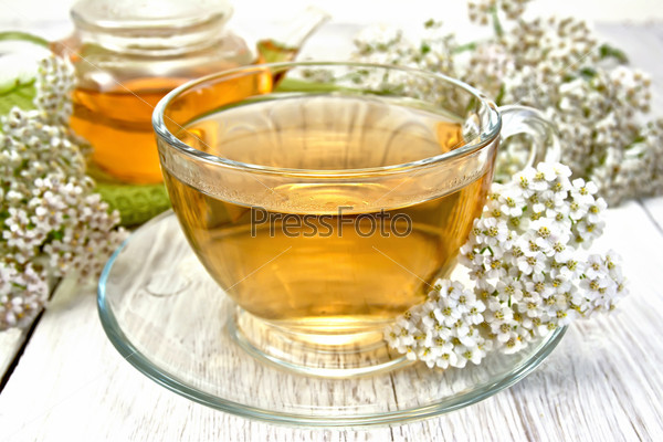Yarrow tea in a glass cup and teapot, fresh yarrow flowers on a background of light board, stock photo