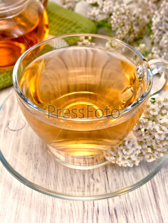 Yarrow tea in a glass cup and teapot, fresh yarrow flowers on a wooden boards background