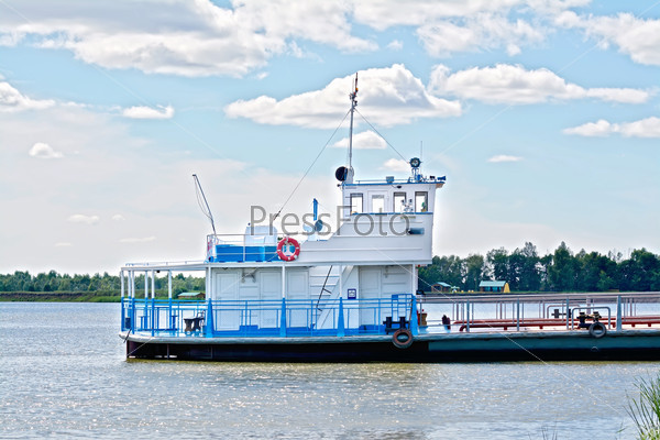 White and blue ferry tug on the background of water, trees, blue sky and white clouds