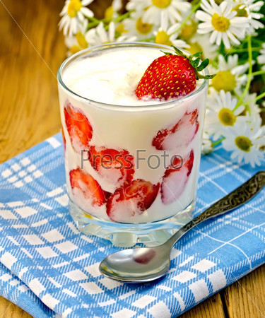 Thick yogurt with strawberries in a glass with a spoon, napkin, a bouquet of daisies on a background of wooden boards
