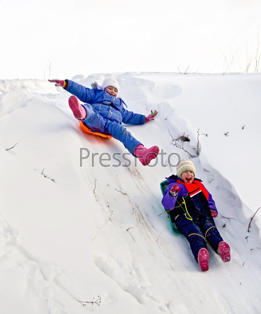 Две маленькие девочки катятся на салазках по снегу с горки