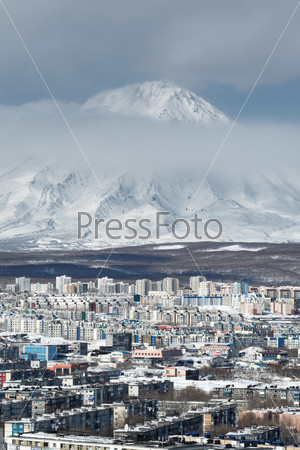 Winter cityscape: top view of City Petropavlovsk-Kamchatsky and active Koryaksky Volcano on a cloudy day. Far East, Russia, Kamchatka Peninsula.