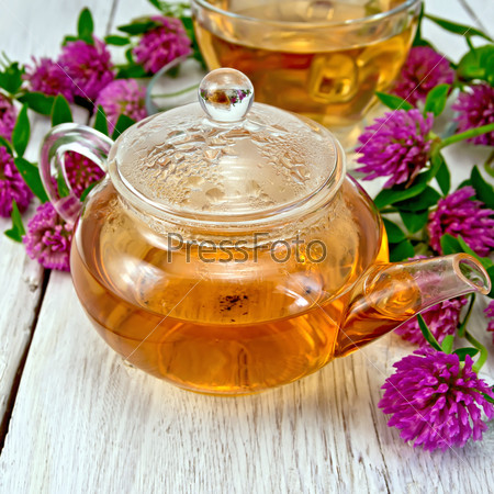 Herbal tea with clover flowers in a glass teapot and cup on the background light wooden boards