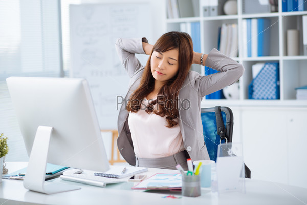 Tired Japanese office worker stretching with her eyes closed