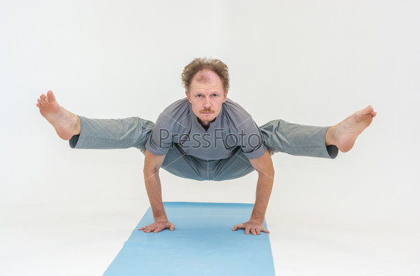 Man performs asanas of Hatha yoga on a blue mat and white background.
