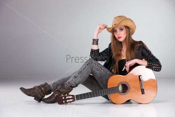 The beautiful girl in a cowboy\'s hat  and acoustic guitar on a gray background