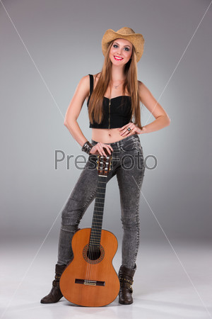 The beautiful girl in a cowboy\'s hat and acoustic guitar on a gray background