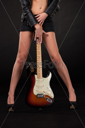 Beautiful young girl\'s legs and hands with electric guitar on a black background.