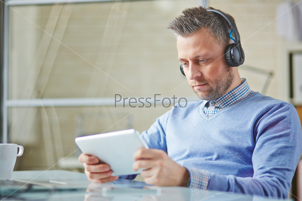 Handsome businessman with earphones using touchpad during break