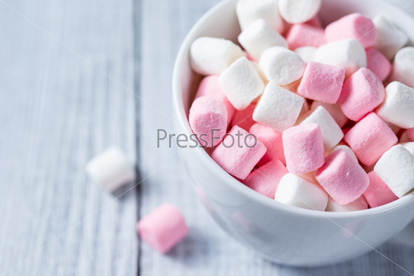 Pink and white marshmallows in a cup, over wood background.