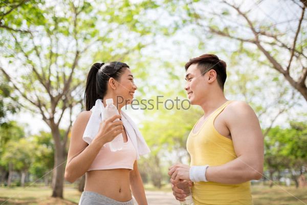 Happy sporty Asian couple with water and towel after exercising in the park