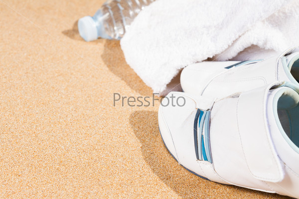 white sneakers in sand  with towel and water