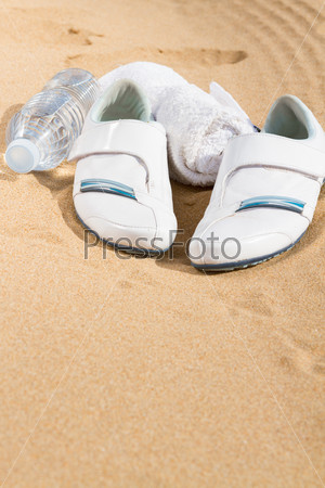white sneakers in sand  with towel and water, with copy space on sand