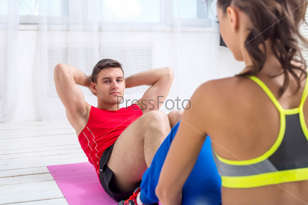 Active sportive man doing abdominal exercises crunches on floor in gym with the help of woman concept training exercising workout fitness aerobic