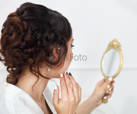 Gentle young bride looks in the mirror