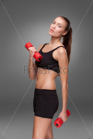 Sporty woman doing aerobic exercise with red dumbbells on grey background
