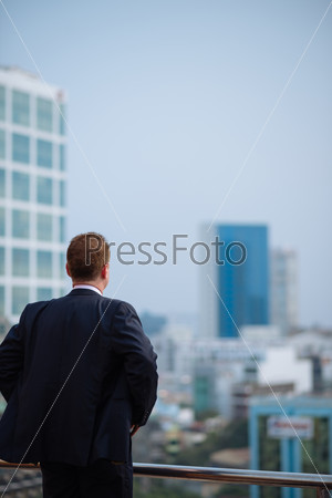 Businessman standing on the roof and looking at the modern city, view from the back