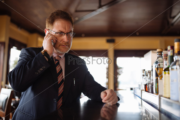 Unhappy mature businessman calling on the phone from the bar