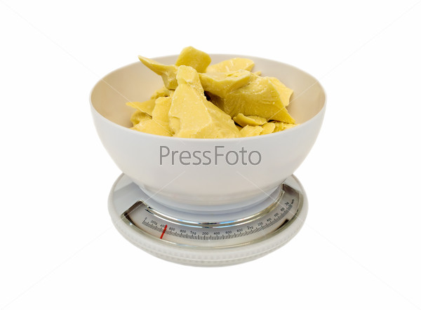 Pieces of natural cocoa butter in the bowl of scales on a white background