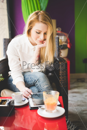 young beautiful blonde straight hair woman in the city sitting at the restaurant using tablet connected online