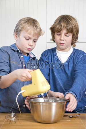 Two friends mixing dough in a stainless steel bowl using a mixer, during a baking workshop for kids at a kitchen counter