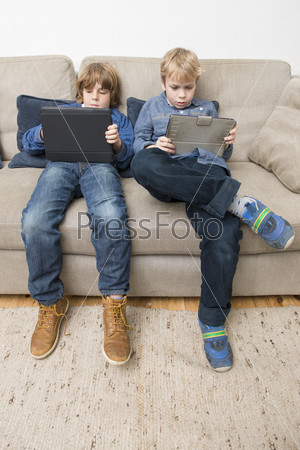 Two boys, playing games on electronic tablets, slouching on a couch, being bored, and acting individualistic
