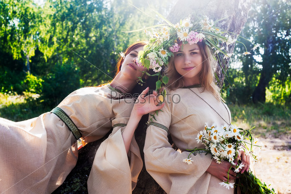 Attractive women in traditional russian clothes relaxes over nature background (Ivan Kupala Holiday Celebration)