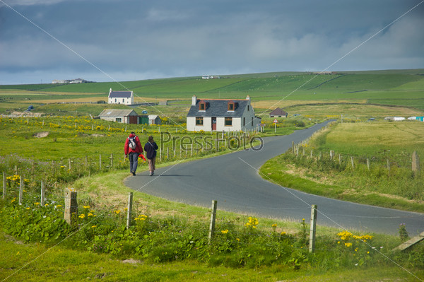 People walking on the road in Scottish landscape in Orkney Island