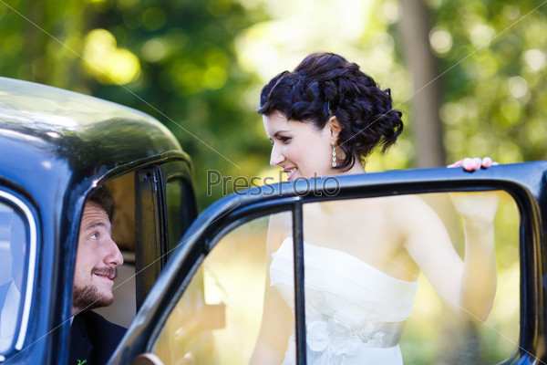 Embrace happy wedding couple inside old car