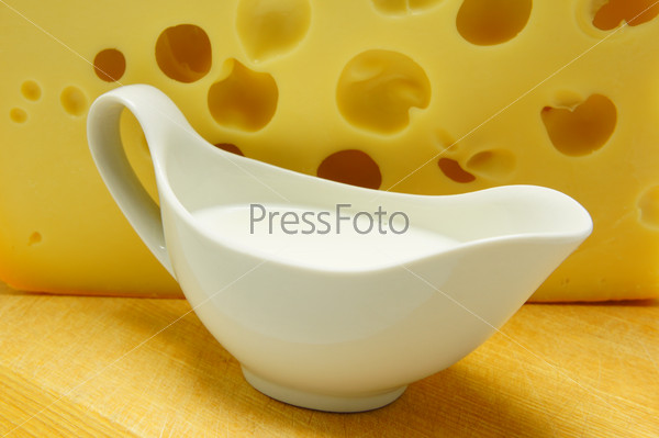 Milk in white milk jug on the background of cheese.