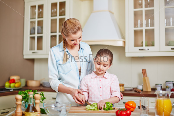 Happy mother and her daughter cooking salad in the kitchen