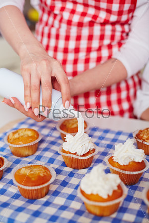 Close-up of young woman decorating baked muffins with whipped cream