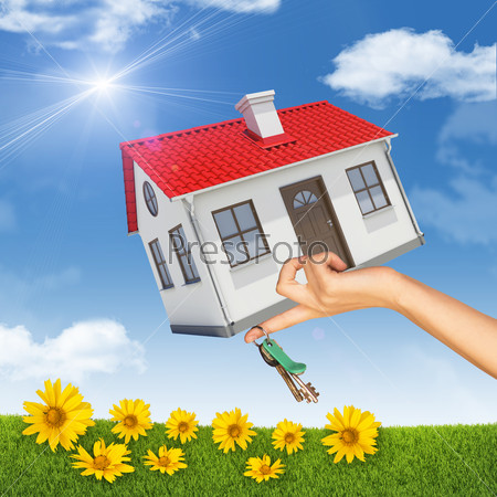 House and bunch of keys in womans hand on nature background with blue sky and yellow flowers