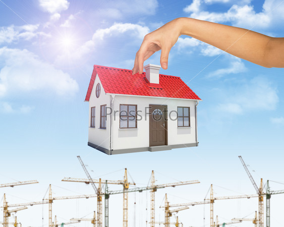 Businesswomans hand holding house for pipe on blue sky background with building cranes, stock photo