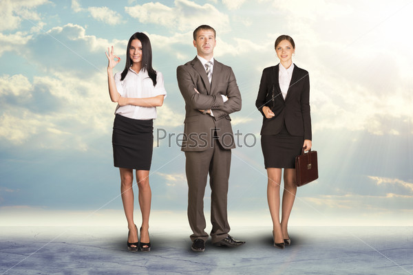 Team leader stands with coworkers in background and in looking at camera on abstract background