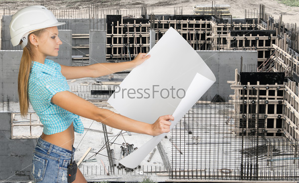 Young woman in hard hat holding map paper looking at camera. Industrial background