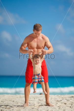 Father and little son having fun on tropical white sand beach near carebbean ocean. Man with little baby boy having fun and playing near the sea water