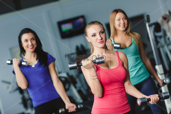 Women working on their triceps with dumbbells at the gym. Image of smiling woman and guy doing lifting exercise with barbells in hands