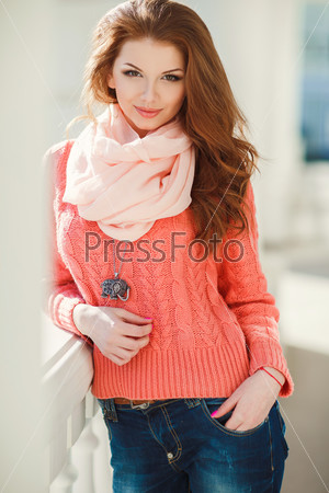 Portrait of beautiful young woman in pink sweater and scarf. Beautiful woman in a sweater in the fall. Portrait of beautiful young woman walking outdoors