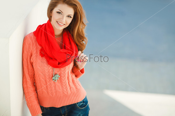 Portrait of beautiful young woman in pink sweater and red scarf. Beautiful woman in a sweater in the fall. Portrait of beautiful young woman walking outdoors in the city