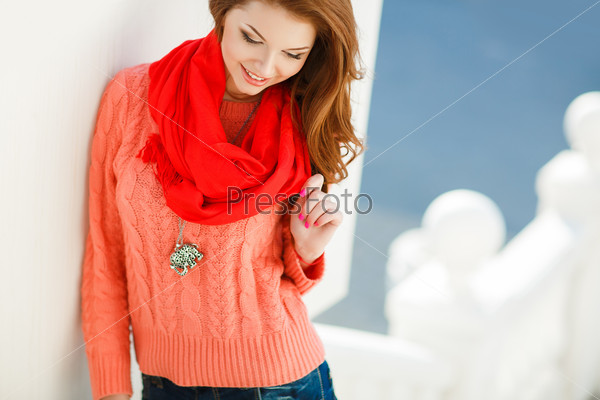 Portrait of beautiful young woman in pink sweater and red scarf. Beautiful woman in a sweater in the fall. Portrait of beautiful young woman walking outdoors in the city