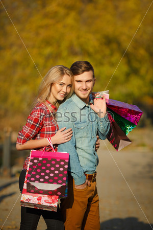 Portrait of happy couple with shopping bags. Couple with paper bags full of presents doing shopping. Outdoor. In park