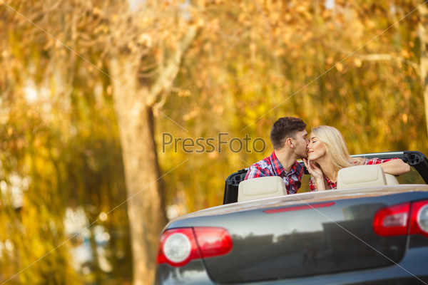 Young hip couple - man and woman - with cabriolet convertible car in summer on a day trip. Couple driving convertible car enjoying a summer day